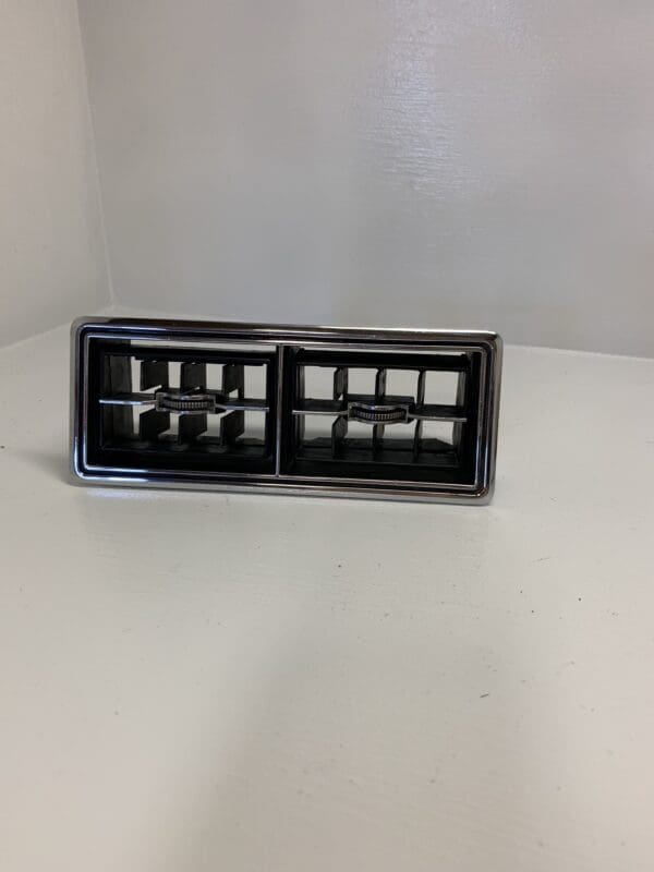 A black and silver car air vent on top of a white table.