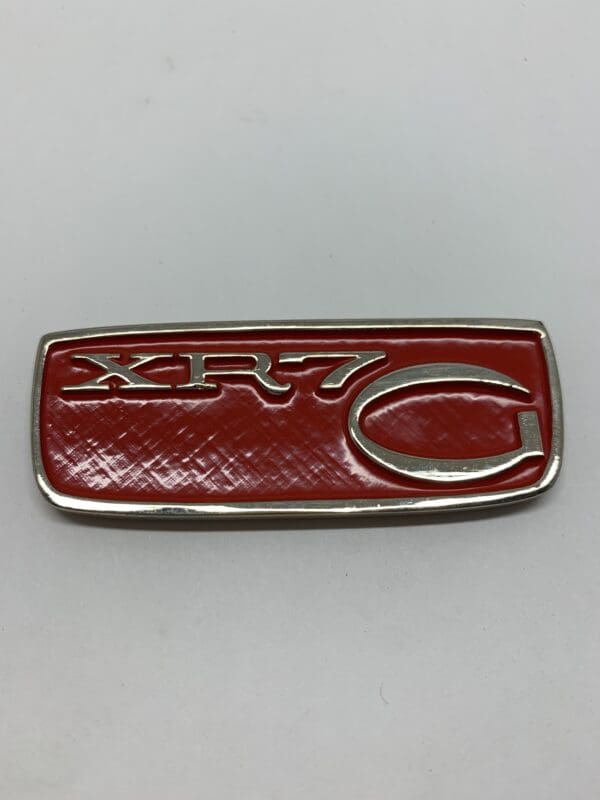 A red and silver car emblem on a white surface.